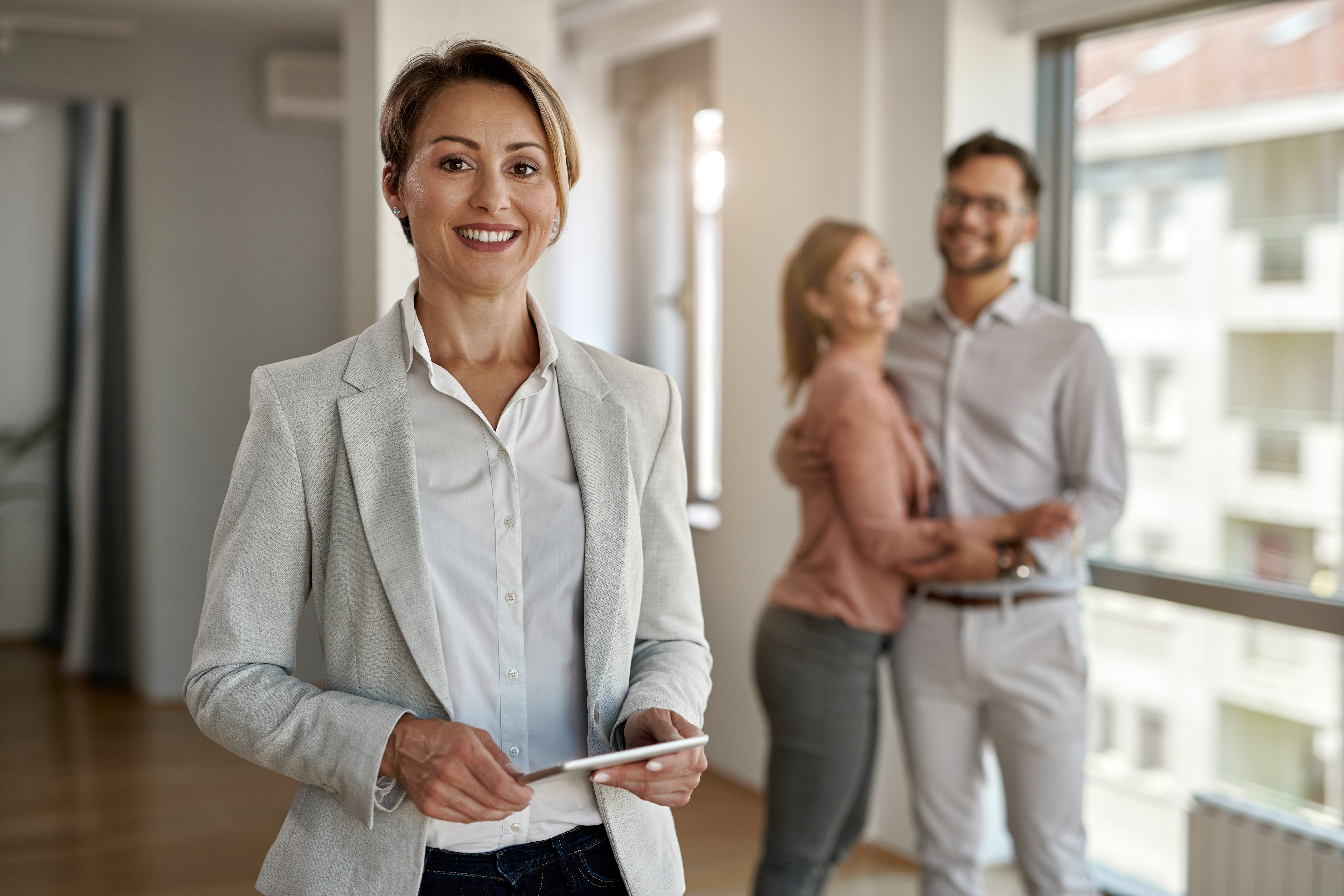 portrait-female-real-estate-agent-looking-camera-while-happy-couple-standing-background